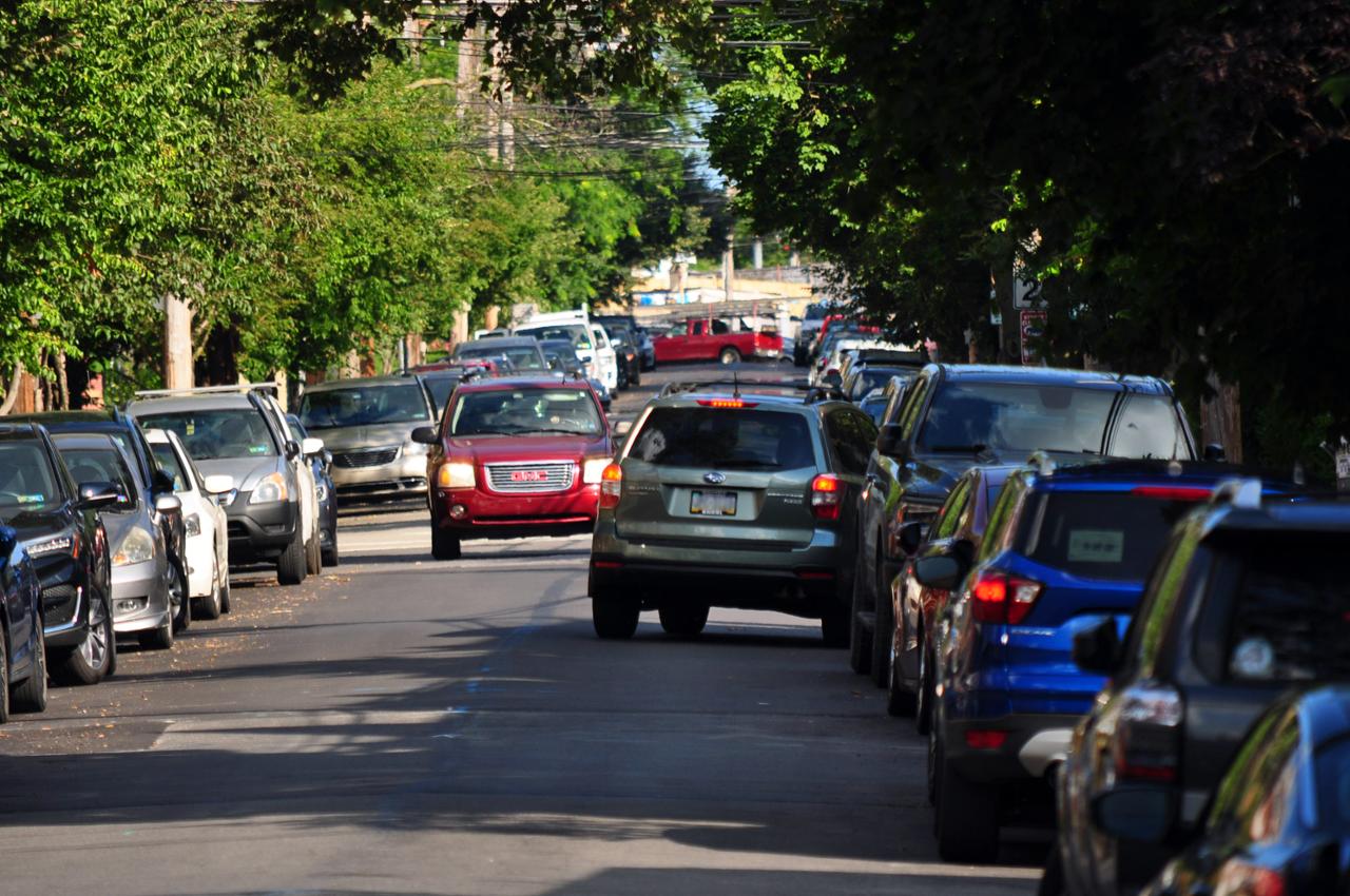  A narrow street with cars on both sides, with two cars attempting to pass