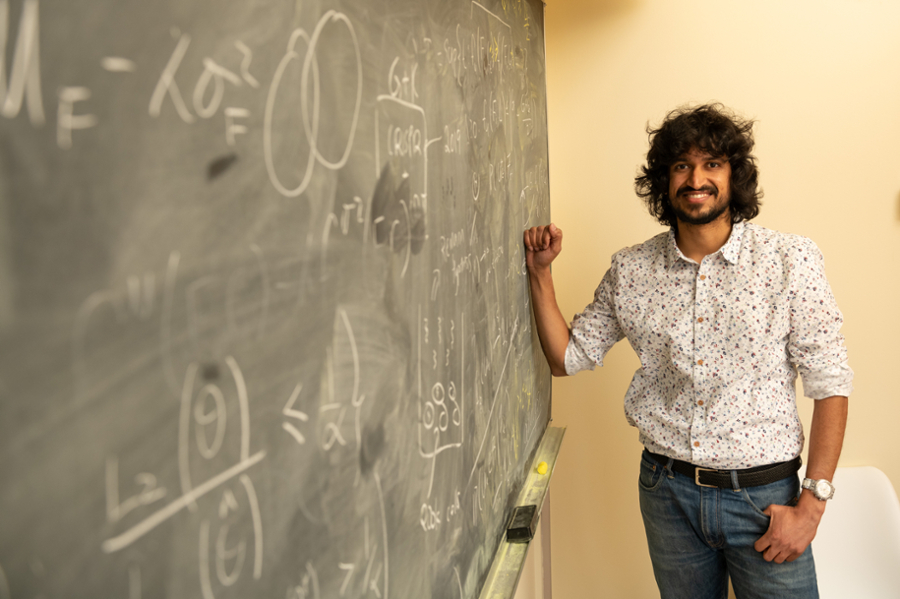  Aaditya Ramdas stands to the right of a black chalkboard covered in scientific formulas.