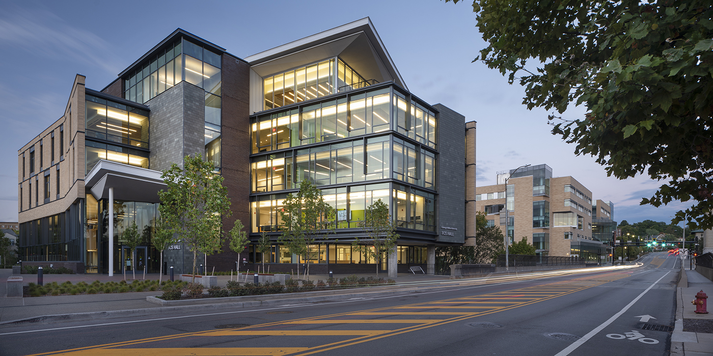 An exterior shot of a multi-storey building set close to a road. The building is a combination of glass and buff brick and some small trees are planted in front of it.